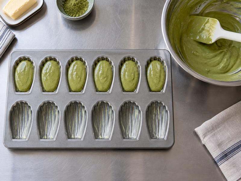 Matcha madeleines batter portioned into shell-shaped metal molds