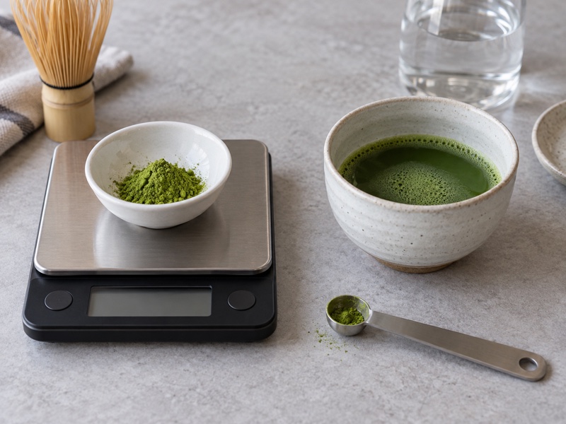 Pure matcha powder on a scale beside an unsweetened cup of matcha