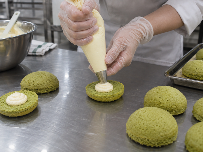 Pale cream piped onto cooled green cake shells for whoopie pie assembly