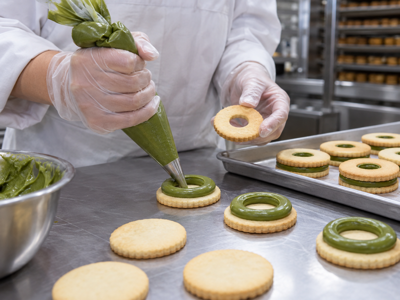 Green matcha filling piped before placing a linzer cookie top