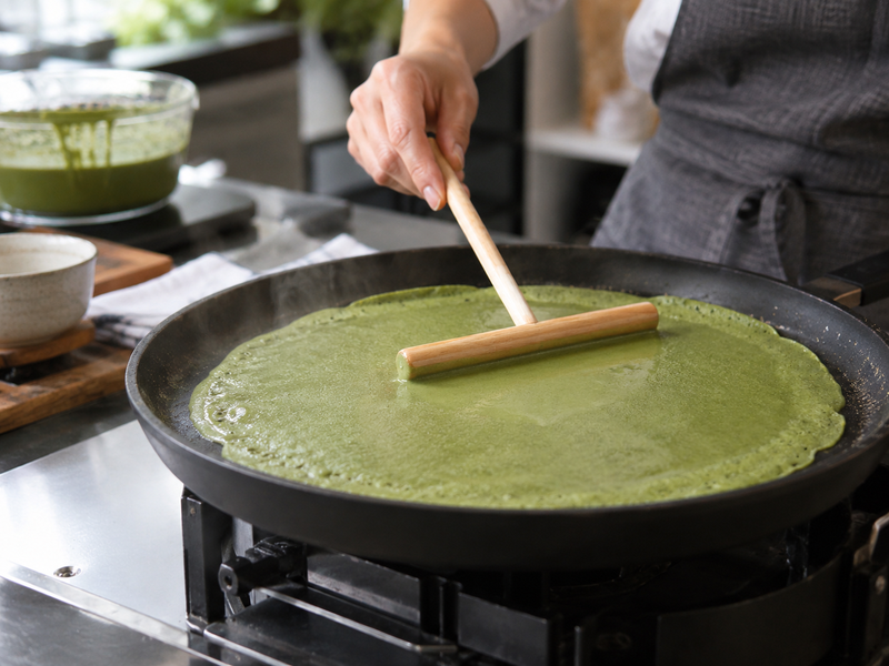 Matcha crepe batter spread thinly on a heated pan