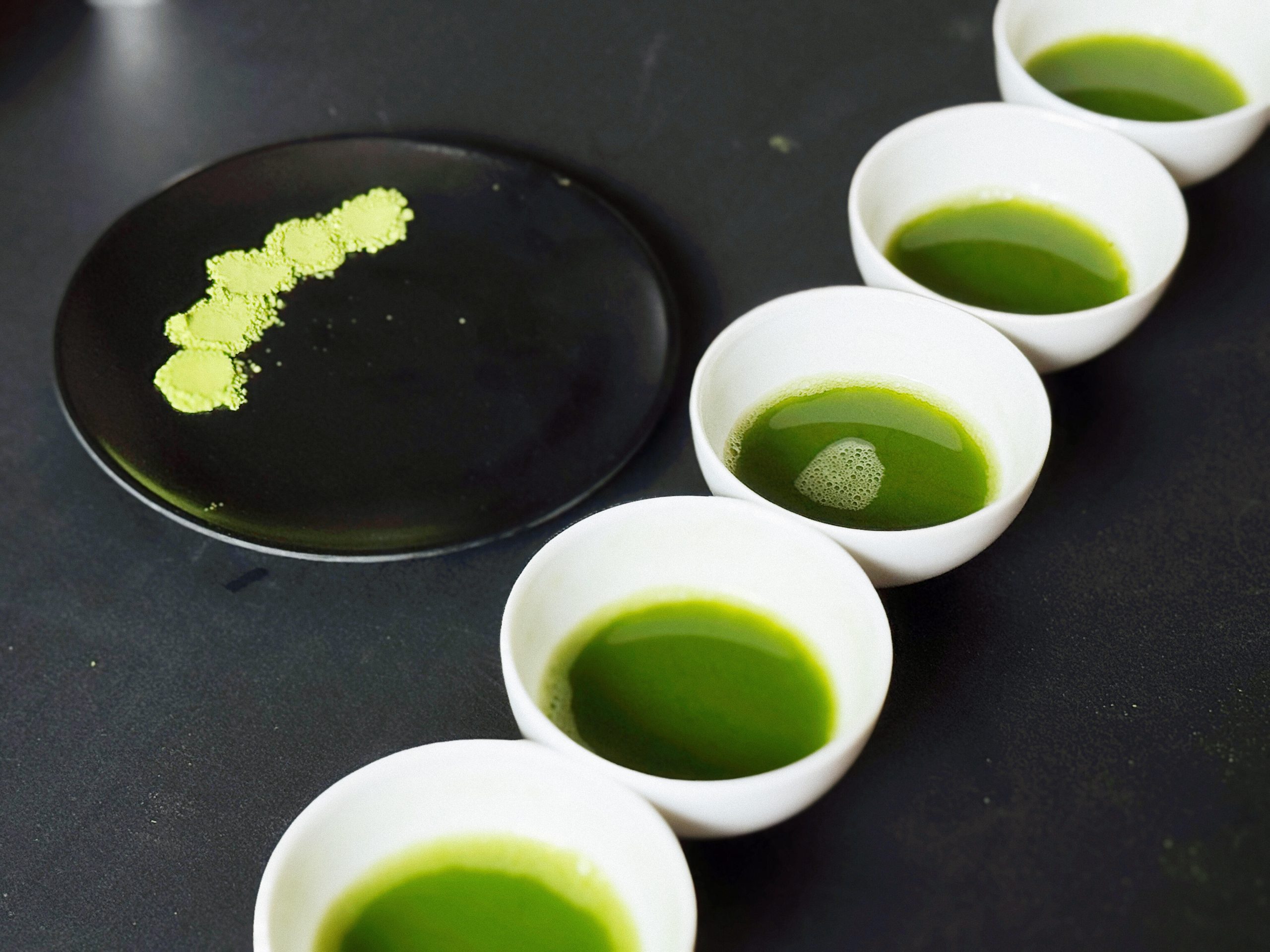Prepared matcha samples in white bowls arranged for side-by-side tasting comparison